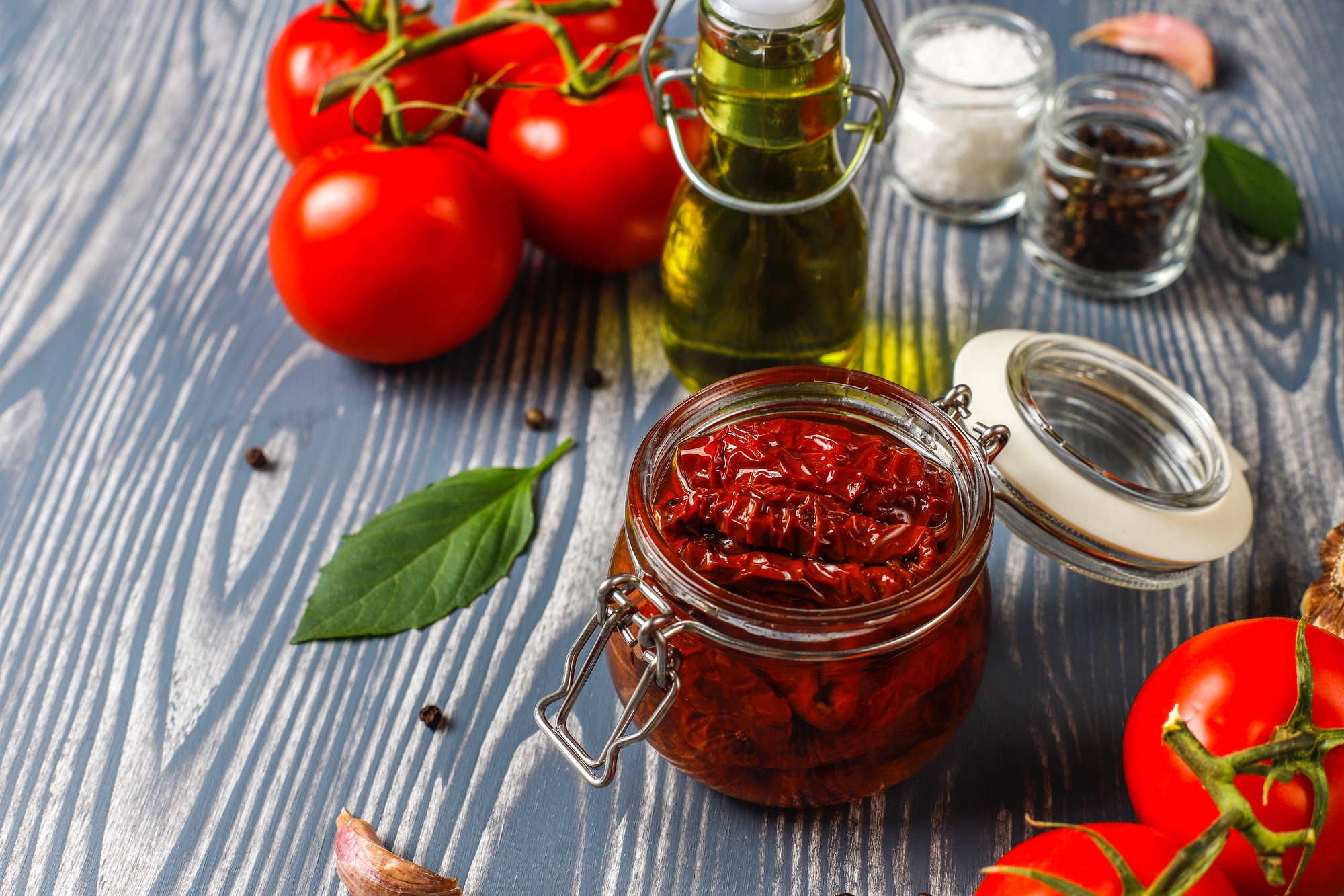 Conserve calabresi di pomodori secchi fatte in casa su tavolo di legno, con pomodori freschi, olio d'oliva, aglio e spezie.